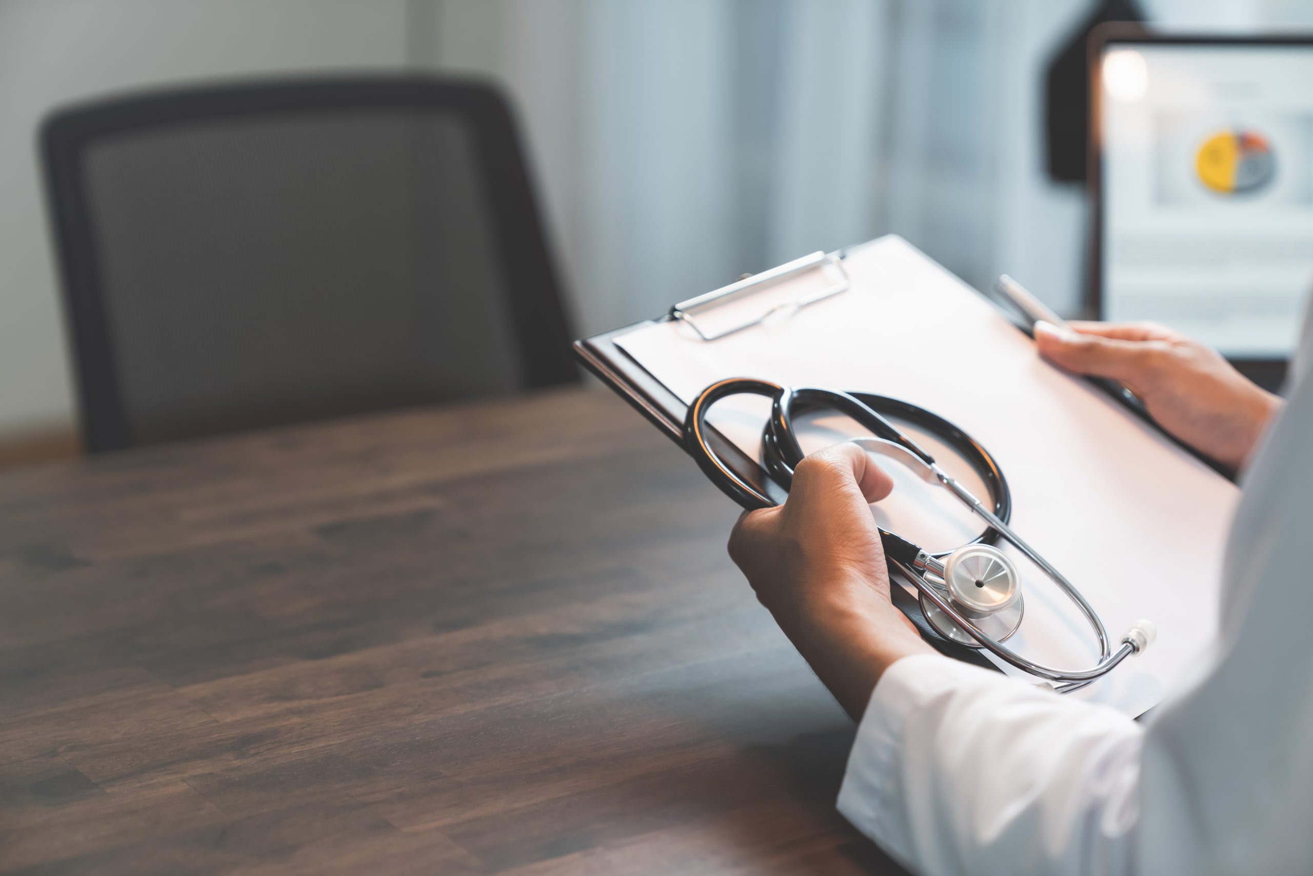 Close up of doctor sitting hands holding stethoscope with chart report at the table, Healthcare and medical.